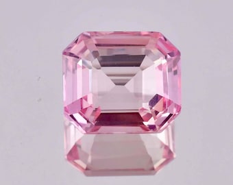 May include: A pink gemstone with a square emerald cut. The gemstone is faceted and has a high level of clarity.