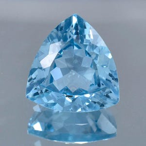 May include: A triangular cut aquamarine gemstone with a light blue colour. The gemstone is faceted and has a high level of clarity.