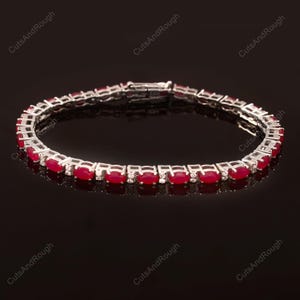 May include: A silver tennis bracelet with a row of oval-shaped red gemstones and smaller clear gemstones.