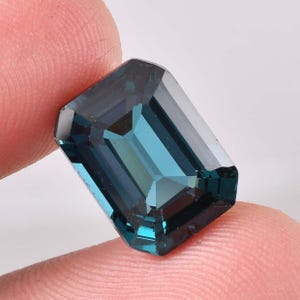 May include: A dark teal emerald cut gemstone with a faceted finish.