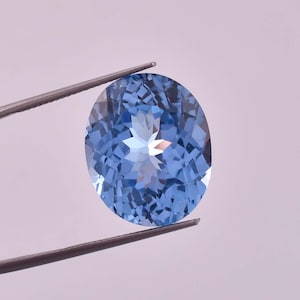 Puede incluir: Una piedra preciosa ovalada de color azul claro con un patrón en forma de estrella en su interior. La piedra preciosa está sujeta por unas pinzas.