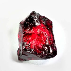 May include: A large, rough, red gemstone with a dark red hue. The gemstone has a natural, unpolished look.
