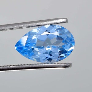 May include: A pear-shaped light blue gemstone held by tweezers. The gemstone is faceted and has a high degree of brilliance.