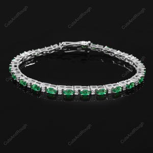 Op de afbeelding: Een tennisarmband met ovale groene edelstenen en kleine ronde witte edelstenen, gezet in een zilveren band.