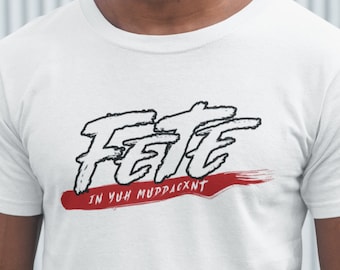May include: White t-shirt with the word "Fete" in a black, stylized font, above the phrase "IN YUH MUDDACXNT" in red, on a red brushstroke. The shirt is a crew neck.