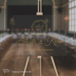 Puede incluir: Un cartel de bienvenida de boda dorado con una corona y las iniciales "AK" en el centro. El cartel dice "A rife & K aan Herzlich Willkommen".