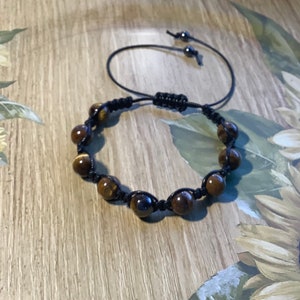 May include: A brown and black beaded bracelet with a black cord. The beads are round and have a tiger's eye pattern.