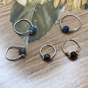 May include: Five wire wrapped rings with different colored stones. The rings are made with silver and gold wire. The stones are blue, black, and gray.