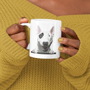 May include: White ceramic mug with a cartoon illustration of a white bull terrier with black spots peeking over the rim of the mug.