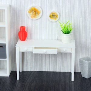 Puede incluir: Conjunto de muebles de casa de muñecas blanco con un escritorio, una estantería, un jarrón, una planta y un cubo de basura. El escritorio tiene un cajón y está hecho de plástico blanco. La estantería tiene seis estantes y también está hecha de plástico blanco. El jarrón es rojo y la planta es verde. El cubo de basura es gris y tiene una superficie texturizada.