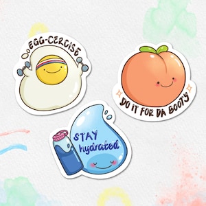 Op de afbeelding: Drie kleurrijke stickers met schattige cartoonfiguren en motiverende zinnen. De eerste sticker heeft een cartoon-ei met halters en de tekst "EGG-CERCISE". De tweede sticker heeft een cartoon-perzik met de tekst "DO IT FOR DA BOOTY". De derde sticker heeft een cartoon-waterdruppel met een waterfles en de tekst "STAY hydrated".