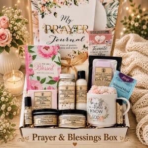 May include: A gift box labeled Prayer & Blessings Box containing a My Prayer Journal, a You Are Blessed devotional, a box of Bible verses, bath salts, body lotion, shower steamers, a mug with text, a candle, sugar scrub, lip balm, and soap.