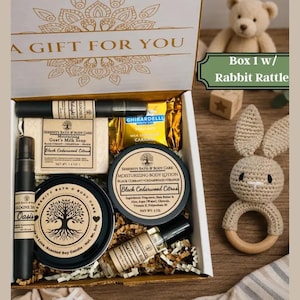 May include: A gift box containing a goat's milk soap bar, a scented soy candle, a moisturizing body lotion, two cologne spray bottles, and a caramel chocolate bar. A crocheted rabbit rattle with a wooden ring sits next to the open box.