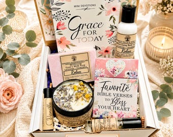 May include: A gift box containing a Mini Devotions Grace for Today book, a bottle of lavender and chamomile body lotion, a bar of goat's milk soap, a candle topped with dried flowers, a vanilla lip balm, and a Favourite Bible Verses book.