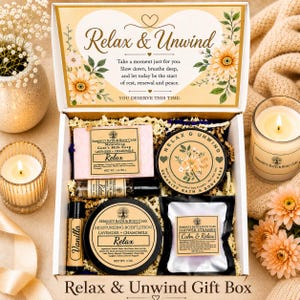 May include: A gift box labeled Relax & Unwind containing a 4 oz bar of lavender and chamomile goat's milk soap, a scented soy candle, a 5 oz container of lavender and chamomile body lotion, a vanilla lip balm, a shower steamer, and a small oil vial.