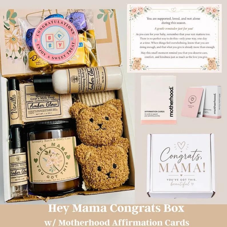 May include: A gift box containing a candle labeled Hey Mama You Got This, a bottle of Amber Glow lotion, a bar of goat's milk soap, a vanilla roll-on, two plush bear-shaped items, a bag of chocolates, and a set of Motherhood affirmation cards.