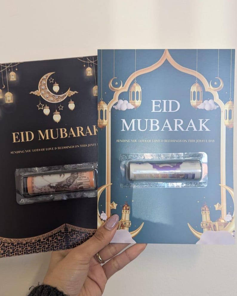 Puede incluir: Dos tarjetas de felicitaci&oacute;n de Eid Mubarak. Una tarjeta es negra con detalles dorados, una luna creciente y faroles. La otra es verde azulado con detalles dorados, faroles y un dise&ntilde;o de mezquita. Cada tarjeta contiene un art&iacute;culo enrollado en una funda de pl&aacute;stico transparente.