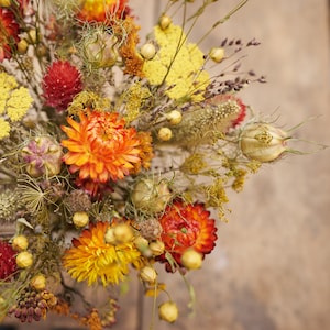 May include: A bouquet of dried flowers in shades of orange, yellow, and brown. The bouquet includes dried wildflowers, grasses, and seed pods.