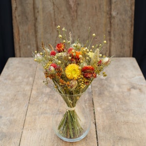 May include: A bouquet of dried flowers in a clear glass vase. The flowers are a mix of yellow, orange, and red.