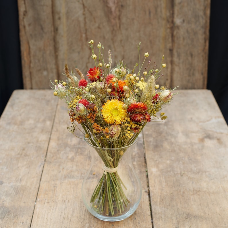 May include: A bouquet of dried flowers in a clear glass vase. The flowers are a mix of yellow, orange, and red.