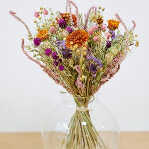 May include: A bouquet of dried flowers in a clear glass vase. The flowers are a mix of purple, pink, orange, and yellow.