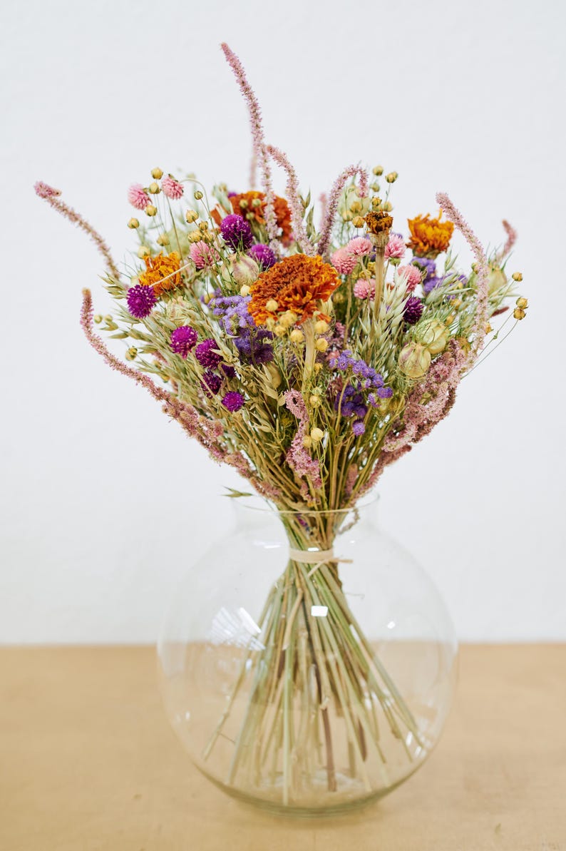 May include: A bouquet of dried flowers in a clear glass vase. The flowers are a mix of purple, pink, orange, and yellow.