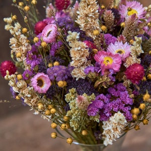 May include: A bouquet of dried flowers in shades of pink, purple, and yellow. The bouquet includes dried grasses and other botanicals.