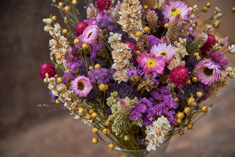 May include: A bouquet of dried flowers in shades of pink, purple, and yellow. The bouquet includes dried grasses and other botanicals.