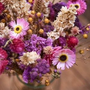 May include: A bouquet of dried flowers in shades of pink, purple, and white. The bouquet includes dried statice, strawflower, and other dried flowers.