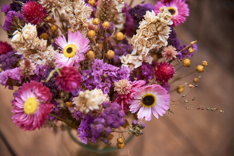 May include: A bouquet of dried flowers in shades of pink, purple, and white. The bouquet includes dried statice, strawflower, and other dried flowers.