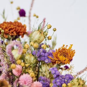 May include: A bouquet of dried flowers in shades of purple, orange, and yellow. The bouquet includes dried lavender, strawflower, and other wildflowers.