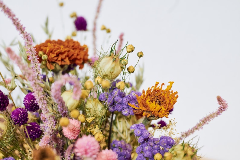 May include: A bouquet of dried flowers in shades of purple, orange, and yellow. The bouquet includes dried lavender, strawflower, and other wildflowers.