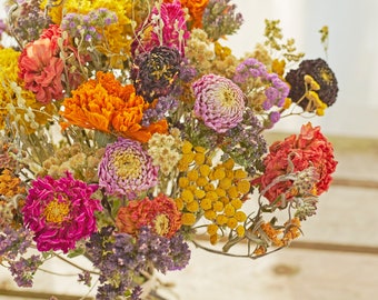 May include: A bouquet of dried flowers in shades of pink, orange, yellow, and purple. The flowers are arranged in a vase and are surrounded by greenery.