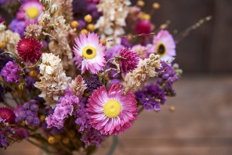 May include: A bouquet of dried flowers in shades of pink, purple, and white. The bouquet includes dried daisies, lavender, and other wildflowers.