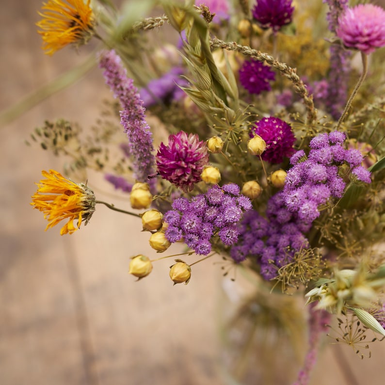 May include: A bouquet of dried flowers in shades of purple, yellow, and orange. The flowers are arranged in a clear glass vase.