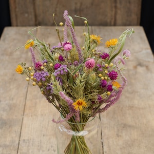 May include: A bouquet of dried flowers in a clear glass vase. The bouquet includes purple, pink, and yellow flowers, as well as dried grasses.