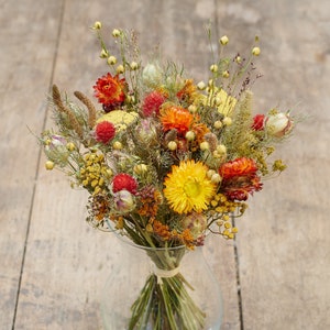 May include: A bouquet of dried flowers in shades of yellow, orange, and red. The flowers are arranged in a clear glass vase.