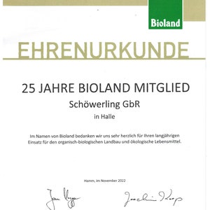 May include: A certificate of honor from Bioland, a German organic farming association, recognizing Sch&ouml;werling GbR for 25 years of membership. The certificate is printed on white paper with green and gold accents. It features the Bioland logo and the text "Ehrenurkunde" in gold lettering.