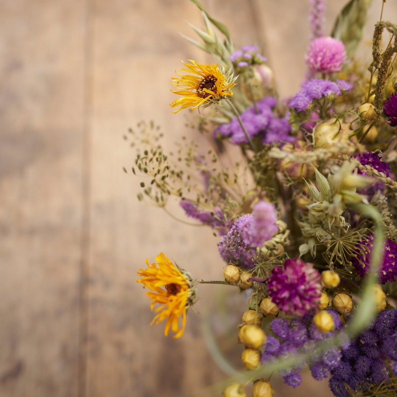 May include: A bouquet of dried flowers in shades of purple, yellow, and brown. The bouquet includes dried sunflowers, lavender, and other wildflowers.