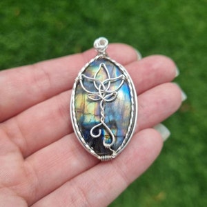 May include: A silver wire wrapped pendant featuring a blue, green, and gold labradorite stone with a silver wire lotus design.