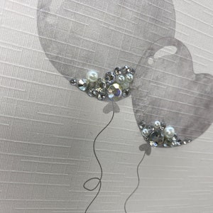 Pu&ograve; includere: Due palloncini grigi a forma di cuore con strass argentati e bianchi su uno sfondo bianco testurizzato.