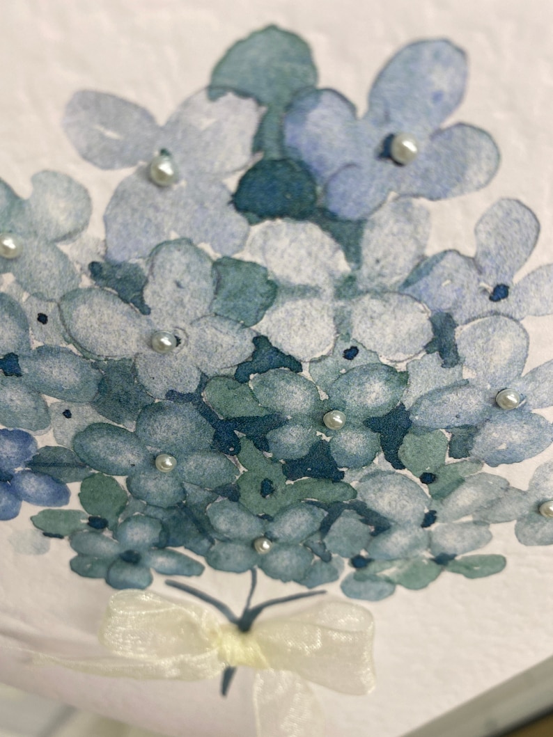 May include: A watercolor painting of a bouquet of blue hydrangeas with white pearl accents and a white satin bow.