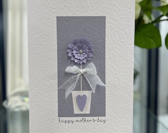 May include: A purple paper flower in a white pot with a heart on the front. The card reads "happy mother's day".