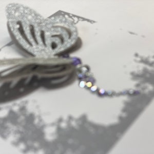 Pu&ograve; includere: Una farfalla argentata con glitter e una catena di perline viola e argento.
