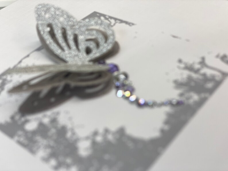 Pu&ograve; includere: Una farfalla argentata con glitter e una catena di perline viola e argento.