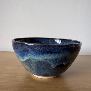May include: A ceramic bowl featuring a deep blue and indigo glaze with mottled textures. The exterior displays a gradient of dark blue transitioning into lighter blue tones, while the interior is a solid dark blue. The base is unglazed white clay.