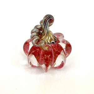 Puede incluir: Una calabaza decorativa de vidrio con cuerpo rojo y transparente y un tallo dorado y plateado. La calabaza tiene un diseño acanalado y probablemente está hecha a mano. Este artículo con temática otoñal es perfecto para la decoración de temporada.