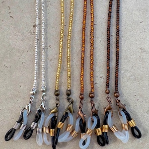 May include: A selection of eyeglass chains in diverse colours, including silver, gold, and brown. Each chain has a beaded design and is attached to black or white rubber loops for securing glasses. The chains have metal clasps.