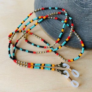 May include: A beaded eyeglass chain with a colorful pattern. The chain features small beads in turquoise, red, black, gold, and yellow. The chain has gold-colored clasps and white rubber loops for attaching to glasses.