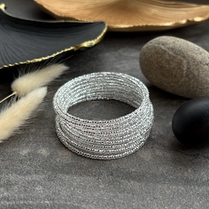 May include: A silver beaded bracelet with multiple strands, stacked and wrapped around each other. The bracelet is on a grey surface.